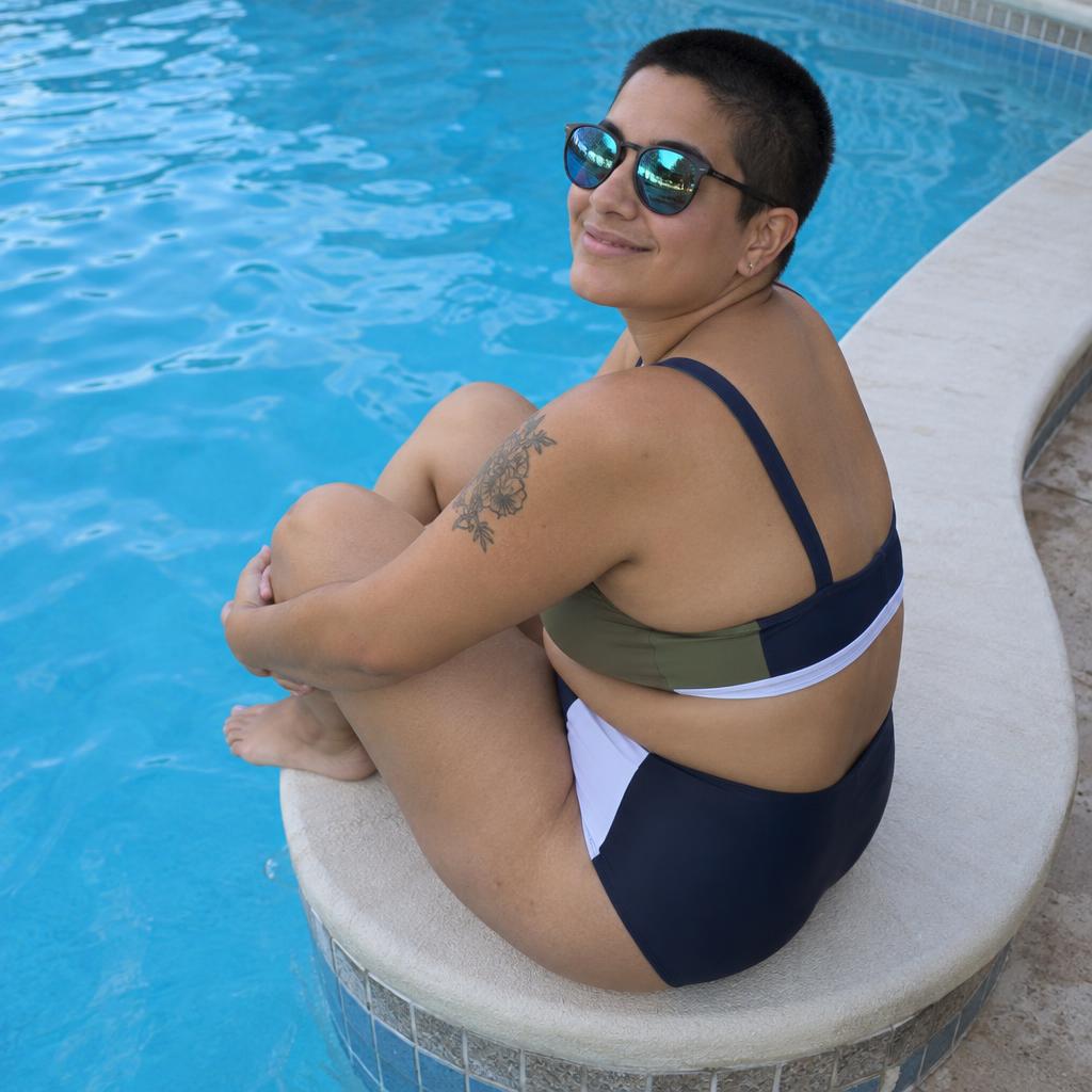 Poolside Summer Post: Direct-flash poolside photo in bright shade: one person perches on a rounded pool corner, knees drawn up, turning to grin at the camera.