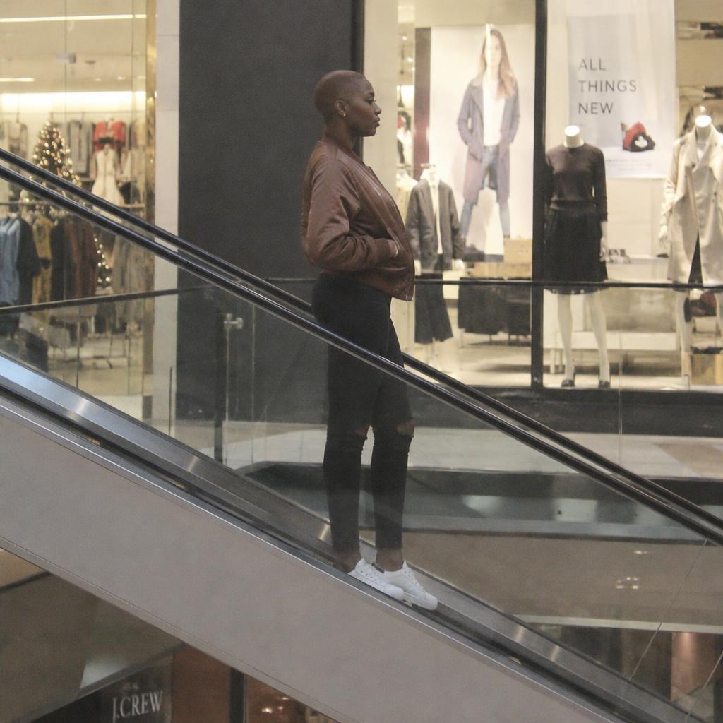 Mall Escalator Streetwear: From across a mall walkway, frame one person head to toe in side profile on an escalator, its diagonal line cutting through a backdrop of…